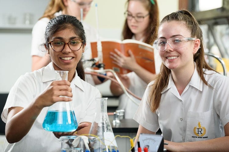 Students holding science equipment and smiling.